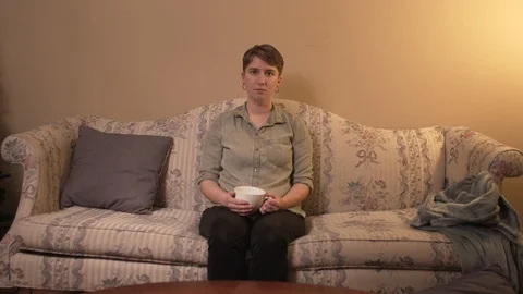 Short haired girl drinking from a mug on a floral couch Stock Footage