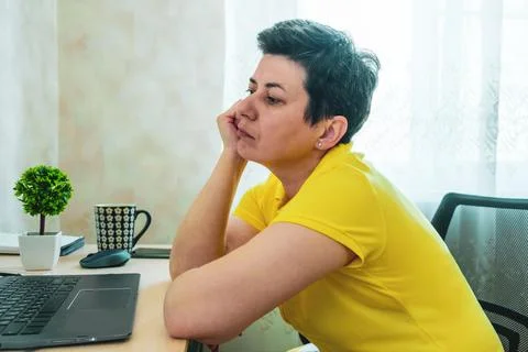 Short-haired, gray-haired brunette woman rests her head on her hand while sit Stock Photos
