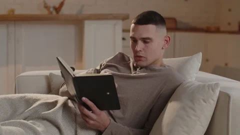 A short-haired man lying on the couch comes up with a list of things to do for Stock Footage 234177571