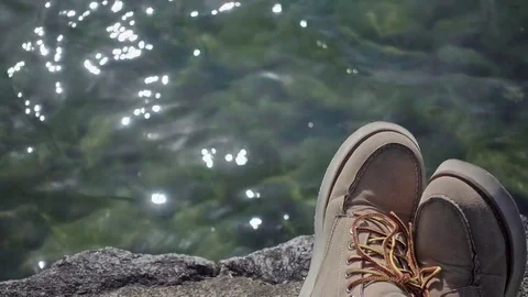 Short rest besides lade - Walking boots overlooking dazzling lake Stock Footage 73961779