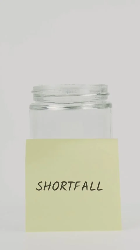 Shortfall text or word on yellow sticky note attached to glass jar with hand Stock Footage 311786179