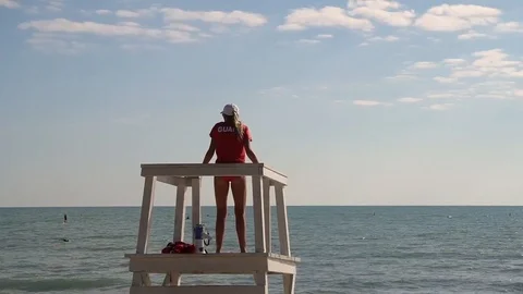 SHOT OF THE BACK OF LIFEGUARD STANDING IN TOWER, SWIMATHON GOING ON IN WATER 스톡 동영상 106131699