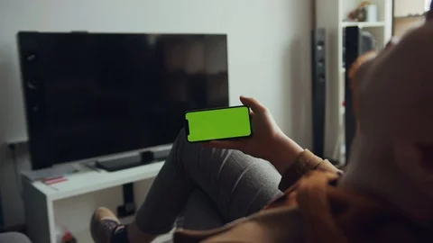 Shot back man use phone with green screen sitting sofa waving his hand talk in Stock Footage 105203919