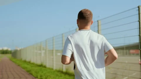 Shot back of young man in white t-shirt running on street at sunlight. Runner Stock Footage 140366033