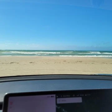 A shot on the beach from behind the windshield of an electric car with sea Stock Photos