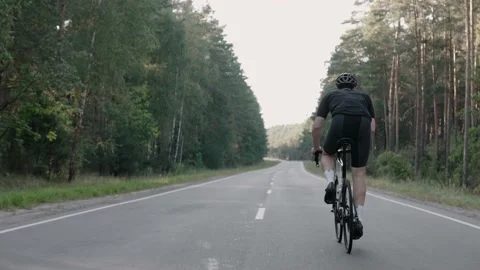 Shot from behind of a man speeding on a road bike in the woods, wearing a helmet Video stock 166174030