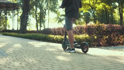 Shot from behind of man standing on electric scooter in park on sunny morning Stock Footage 137646048