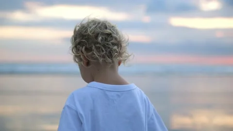 Shot from behind. A small blond child with an angelic appearance walks along the Stock Footage 220106472