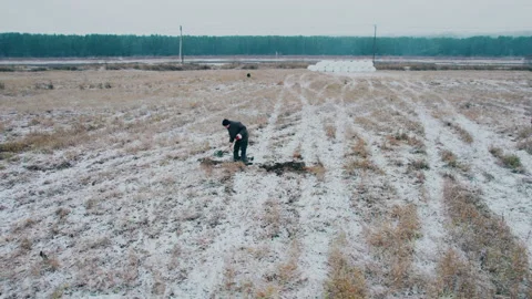 Shot on a drone. A man digs the ground with a shovel in a snow-covered field. Video stock 221164848