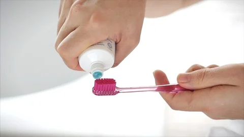 Shot of female hands squeezing colored toothpaste onto a pink toothbrush. Oral Stock Footage 127775740