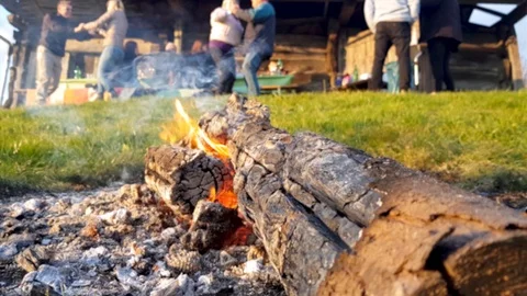 A shot of a fire made in front of a lodge with people dancing at the background Stock Footage 98622630