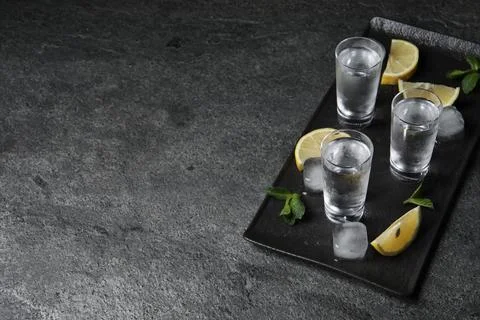 Shot glasses of vodka with lemon slices, mint and ice on grey table. Space .. Stock Photos