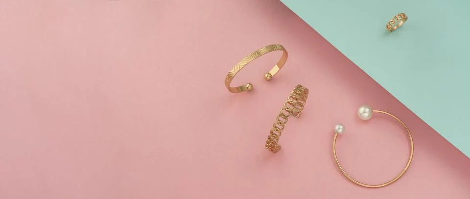 Shot of golden bracelets and ring on pastel colors background with copy space Stock Photos