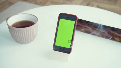 Shot of green screen template smartphone at home, gadget on the table. Cup of Stock Footage 153615757
