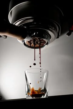 Shot of hot coffee drink is pulled through portafilter into clear glass. Stock Photos