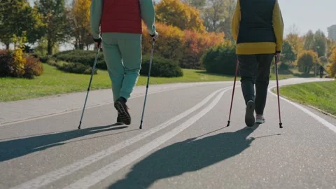 Shot of legs of two people doing Scandinavian walking in fall park, back view Видео 165306807