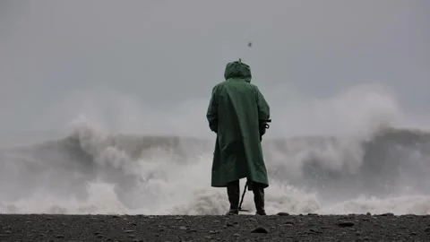 Shot of a man using a metal detector on the beach during a strong storm at sea Stock Footage 300033453