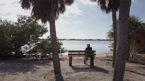 Shot of Palm trees and old man with a hat Sitting on bench. Stock Footage 260644880