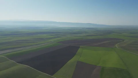 A shot of patterned green and brown farmland stretching out under a clear sky. Stock Footage 334526898