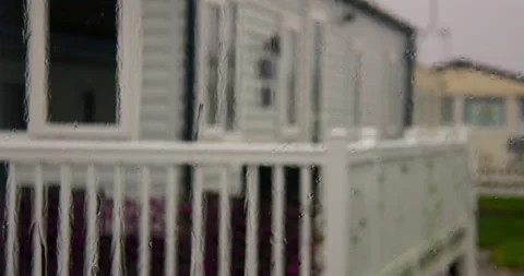 Shot of rain on a static caravan window with static caravans in background at Stock Footage 346814365