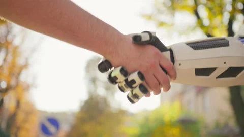 Shot of robot shaking human hand on blurred background of autumn park in Stock Footage 231239495