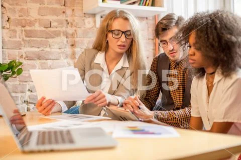 Shot of three young people discussing something with graphincs in their hands Stock Photos