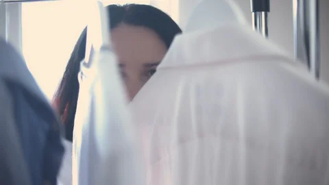 Shot through the racks with clothes of young attractive woman looking for a Stock Footage 127202393
