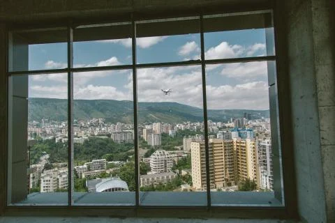 Shot throw the window white drone with camera flying near house, cityscape Stock Photos