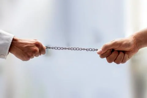 Shot of two hands on the end of a rusted metal chain pulling from both sides  Stock Photos