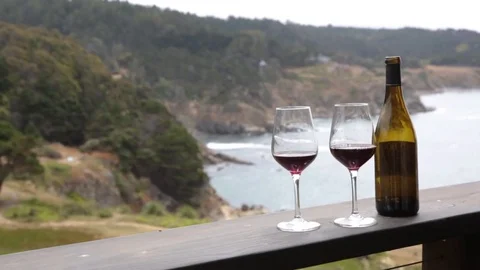 Shot of two wine glasses with empty bottle on resort balcony facing ocean Video stock 79549558