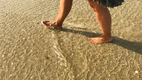 Shot of a woman's legs walking from left to right along the edge of the beach Stock Footage 197767190