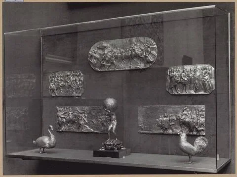 Showcase with metal objects: plaques, an atlas figure and two bird figures... Stock Photos