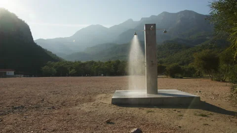 Shower column stands alone on beach, water flows from shower. Mountains and sun Stock Footage 230053442