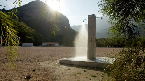 Shower column stands alone on beach, water flows from shower. Mountains and sun Stock Footage 230613864