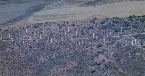 Showing midground band of white posts stretching across arid shrubland with rock Stock Photos