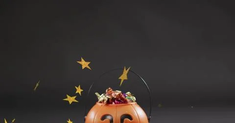 Showing orange jack-o'-lantern bucket holding foil candies on dark table, black Stock Photos