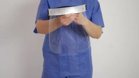 Showing transparent plastic face shield in hands in blue medical suit Stock Footage 136374499