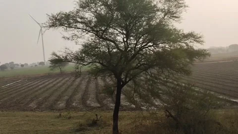 Showing wide green fields, trees, and large wind turbines in the distance. The h Stock Footage 321813390