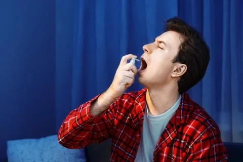 Shows a sick man using throat spray medicine for cold and flu treatment. Ho.. Stock Photos