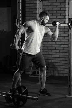 Shredded bodybuilder with a beard is doing biceps curls with dumbbells in a g Stock Photos