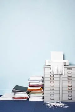 Shredder on file cabinet stack of paperwork on floor in office Stock Photos