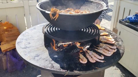Shrimp and crabs cooked on round cast-iron outdoor grill with fire in middle Stockbeeldmateriaal 201167181