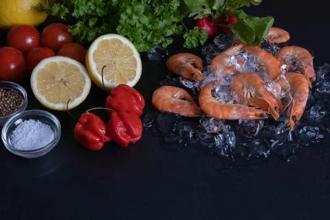 Shrimp are on the table next to pepper, greens, lemon Stock Photos
