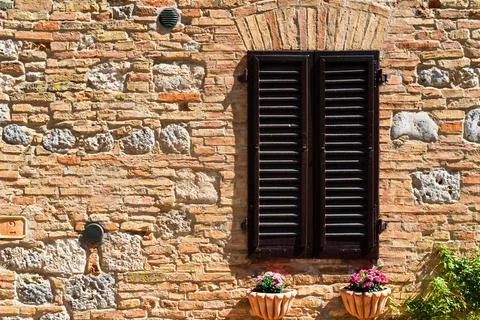 Shuttered window on an aged brick wall, adorned with vibrant flower pots under Fotos de archivo