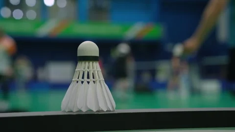 Shuttlecock stands on table against blurred athletic man Видео 294397394