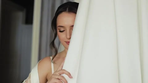 Shy bride hiding behind wedding dress gently touching fabric and slowly lifting Stock Footage 326202541