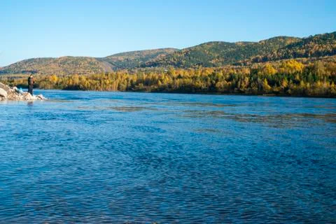 Siberian river and mountains covered by forest with a fisherman in the backgr Stock Photos