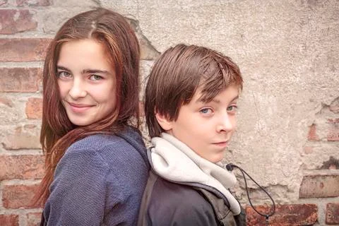 Siblings back to back in front of an old brick wall Stock Photos