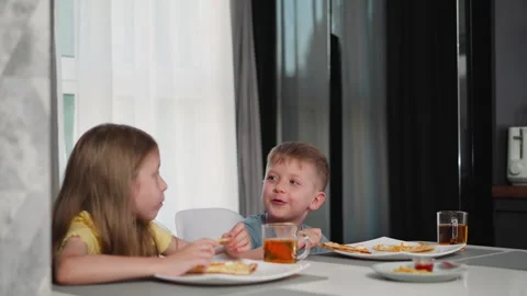 Siblings eating breakfast laughing and chatting at dining table with natural Stock Footage 306623192