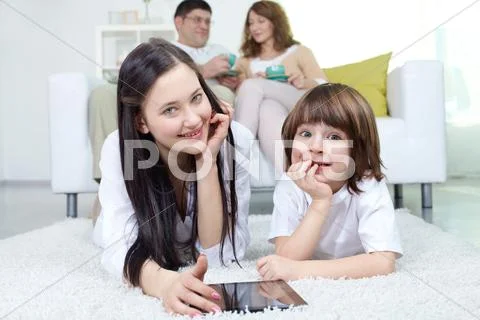 Siblings looking at camera with their parents sitting on sofa at background Stock Photos